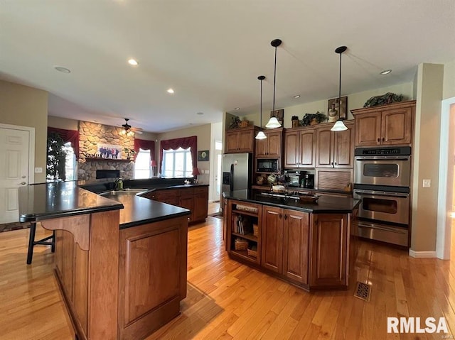 kitchen with a center island, a stone fireplace, hanging light fixtures, light hardwood / wood-style flooring, and appliances with stainless steel finishes