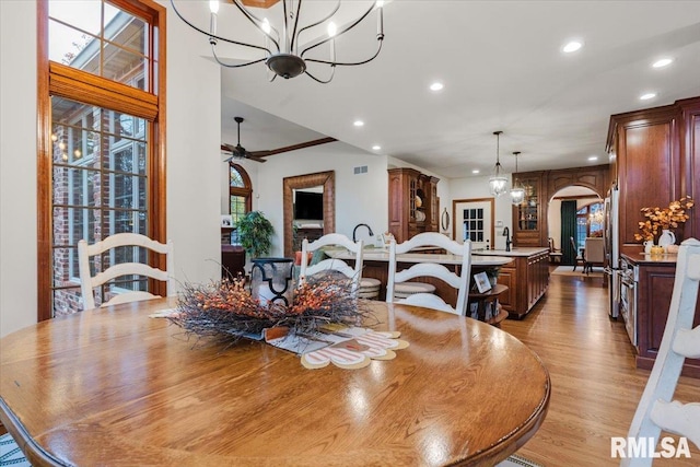 dining space with ceiling fan with notable chandelier, light wood-type flooring, and sink