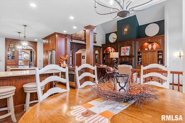 dining area featuring a chandelier, light wood-type flooring, decorative columns, and lofted ceiling