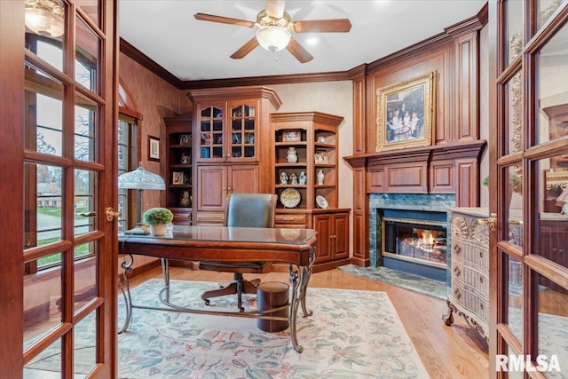 home office with french doors, ornamental molding, ceiling fan, a fireplace, and light hardwood / wood-style floors