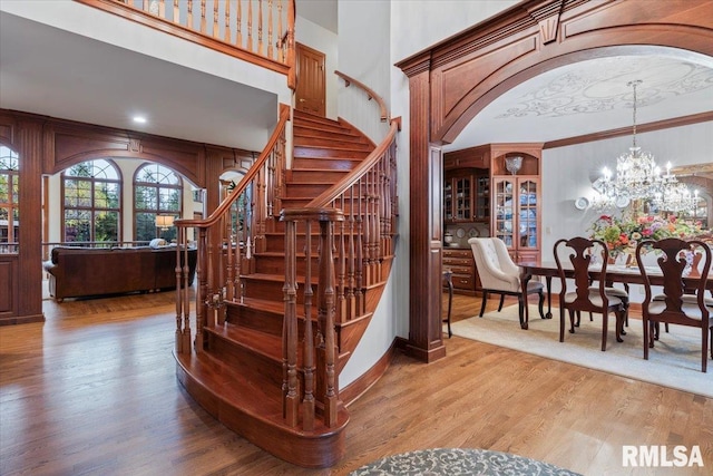 staircase featuring wood-type flooring, a towering ceiling, crown molding, and a notable chandelier