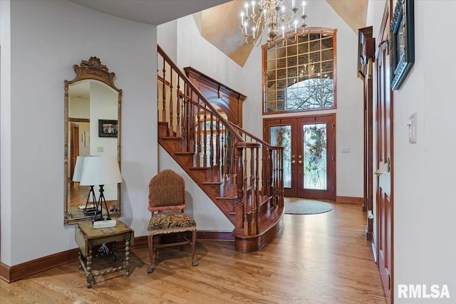 foyer with a notable chandelier, light hardwood / wood-style floors, a towering ceiling, and french doors