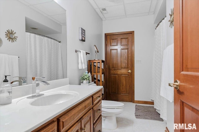 bathroom with tile patterned flooring, vanity, a drop ceiling, and toilet