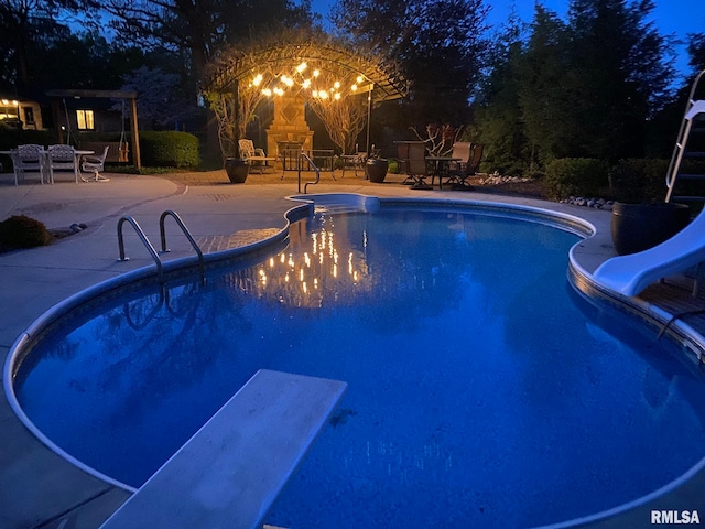 pool at twilight featuring a diving board, a patio area, and a water slide