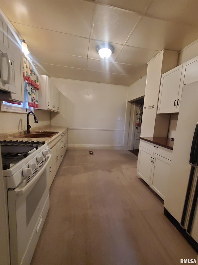 kitchen with white cabinetry, sink, a drop ceiling, white appliances, and light carpet