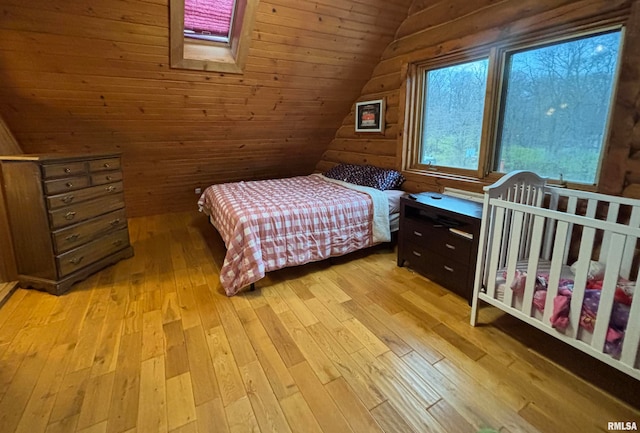 bedroom with vaulted ceiling with skylight, light hardwood / wood-style floors, wood ceiling, and wooden walls