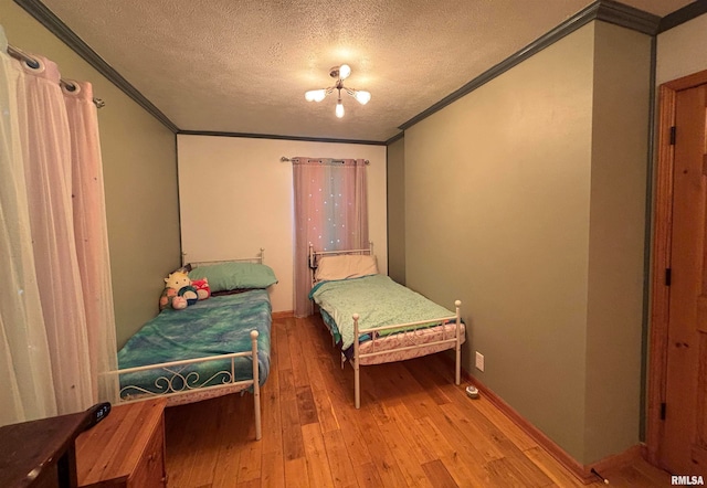 bedroom with a notable chandelier, light hardwood / wood-style floors, a textured ceiling, and ornamental molding