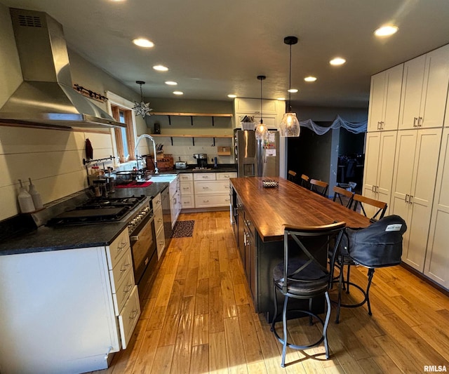 kitchen with wall chimney exhaust hood, stainless steel appliances, a kitchen island, white cabinets, and light wood-type flooring