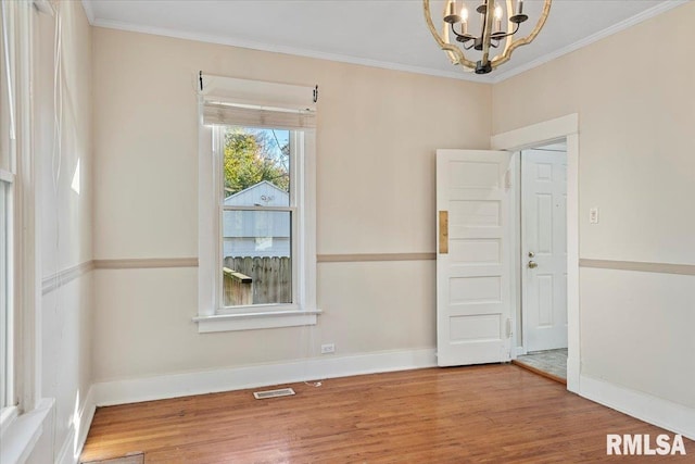 empty room featuring wood-type flooring, an inviting chandelier, and ornamental molding