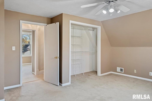 unfurnished bedroom featuring a textured ceiling, light colored carpet, vaulted ceiling, ceiling fan, and a closet