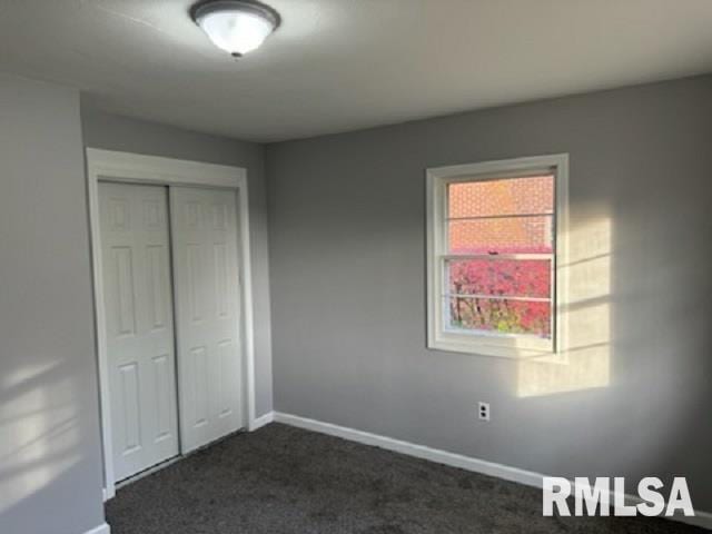 unfurnished bedroom with a closet and dark colored carpet