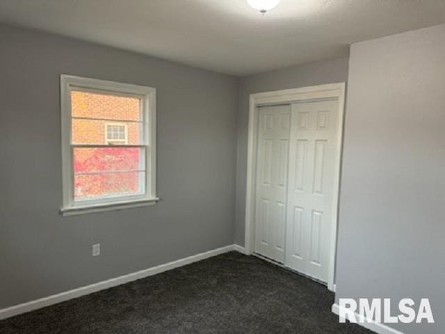 unfurnished bedroom with dark colored carpet and a closet