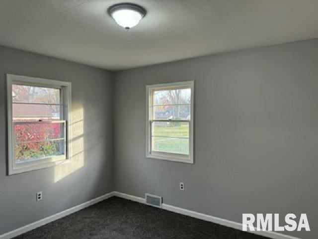 empty room with dark colored carpet and a wealth of natural light