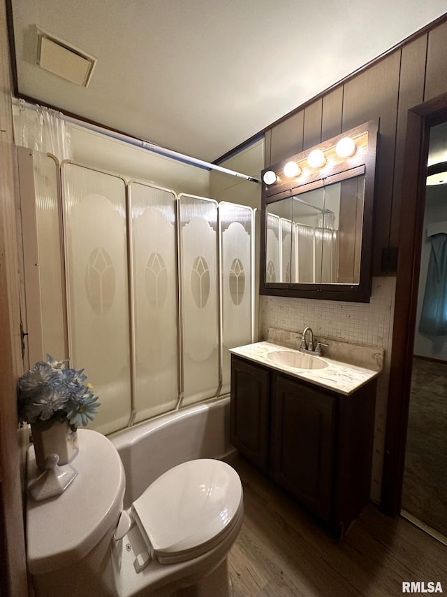 full bathroom featuring toilet, decorative backsplash, hardwood / wood-style floors, enclosed tub / shower combo, and vanity