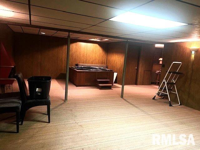 basement featuring a paneled ceiling, wooden walls, and light carpet