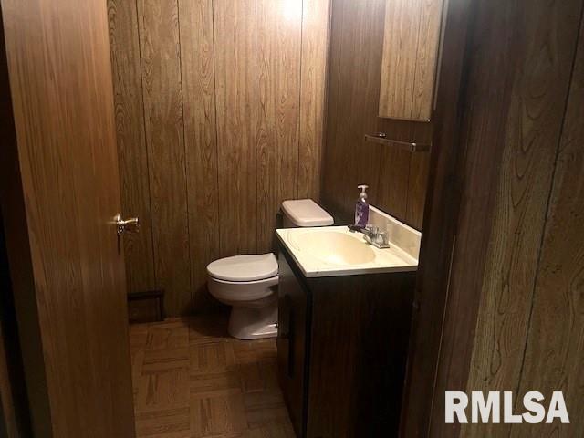 bathroom with parquet flooring, vanity, toilet, and wooden walls