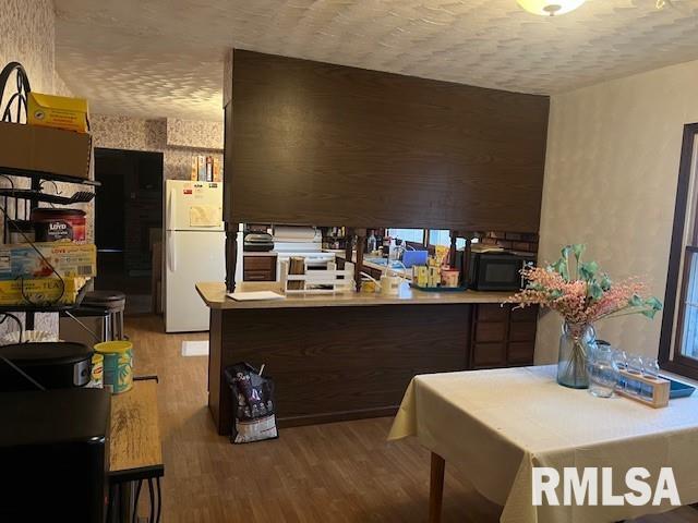 kitchen with kitchen peninsula, white fridge, and hardwood / wood-style flooring