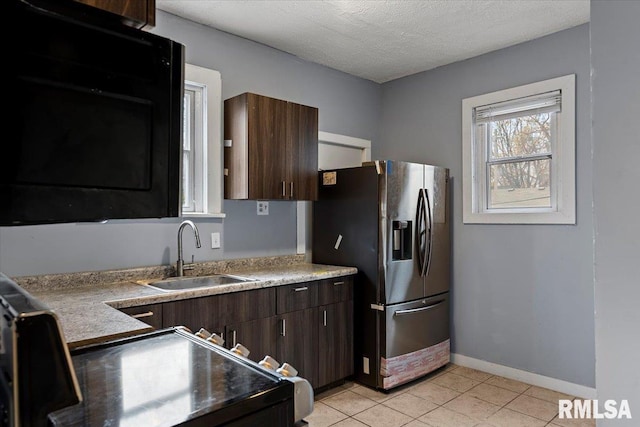 kitchen featuring stainless steel refrigerator with ice dispenser, light tile patterned floors, dark brown cabinets, and sink