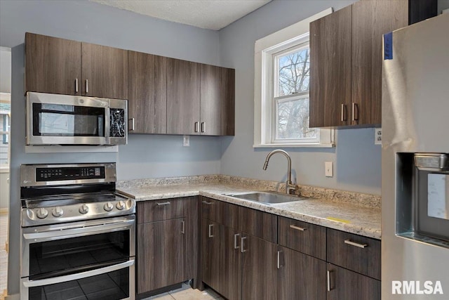 kitchen featuring appliances with stainless steel finishes, light stone counters, dark brown cabinetry, sink, and light tile patterned floors