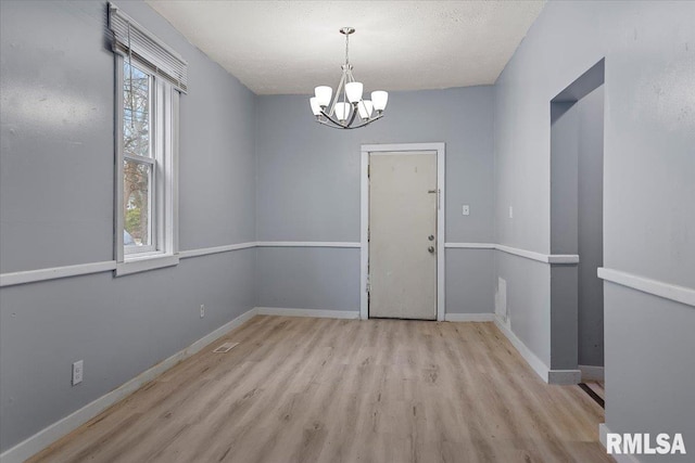 empty room featuring a textured ceiling, light hardwood / wood-style flooring, and an inviting chandelier