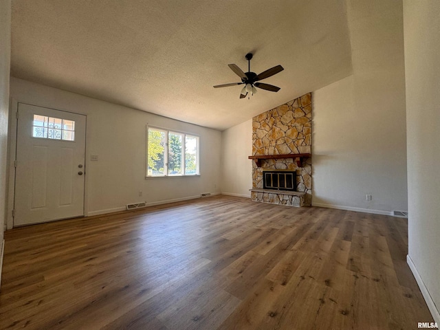 unfurnished living room featuring a textured ceiling, a stone fireplace, wood-type flooring, and vaulted ceiling