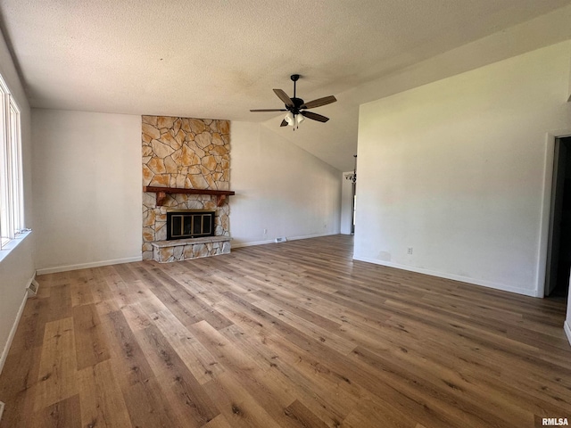 unfurnished living room with wood-type flooring, a stone fireplace, a wealth of natural light, and lofted ceiling