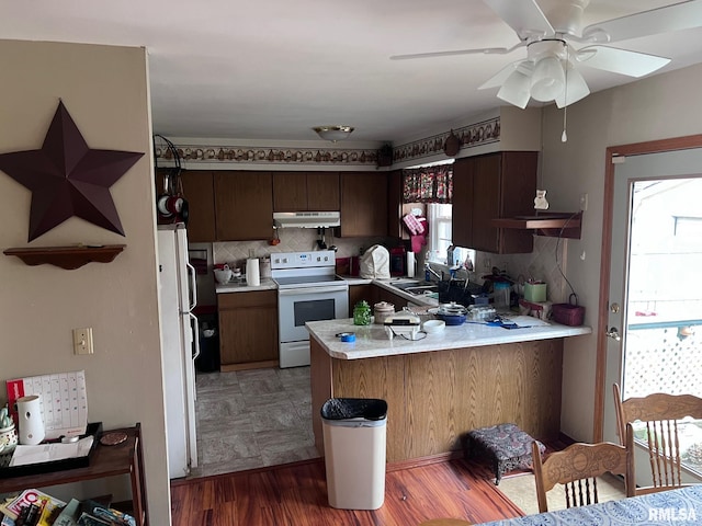 kitchen with kitchen peninsula, backsplash, white appliances, ceiling fan, and dark hardwood / wood-style floors