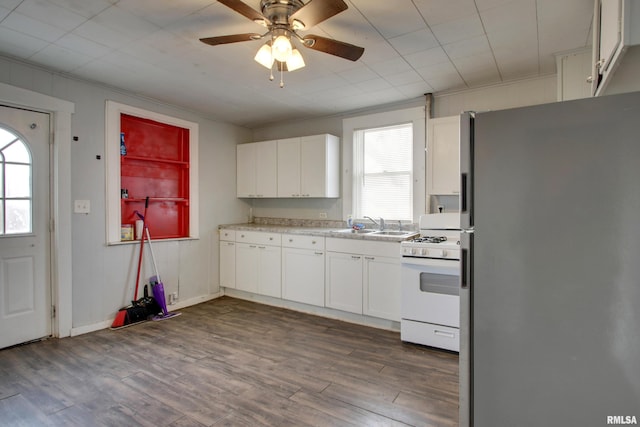 kitchen with white gas stove, stainless steel fridge, white cabinetry, and a wealth of natural light