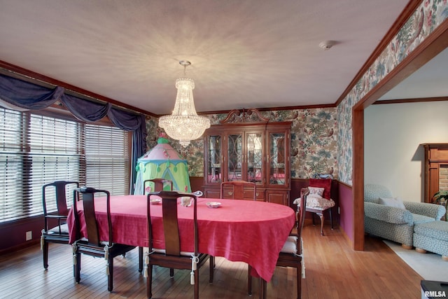 dining area with hardwood / wood-style flooring, crown molding, and an inviting chandelier