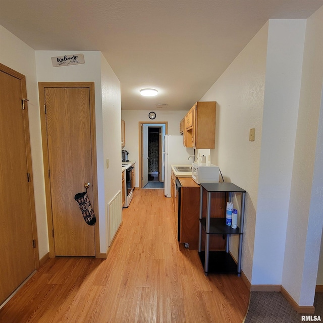 kitchen with white appliances, light wood-type flooring, and sink