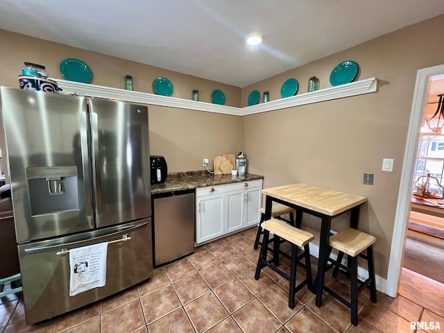 kitchen featuring light tile patterned floors, stainless steel appliances, white cabinetry, and dark stone countertops