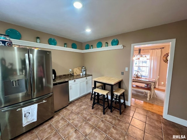 kitchen with appliances with stainless steel finishes, tile patterned floors, dark stone countertops, white cabinets, and hanging light fixtures