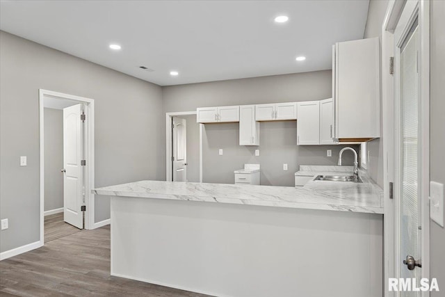 kitchen featuring sink, light stone counters, kitchen peninsula, wood-type flooring, and white cabinets