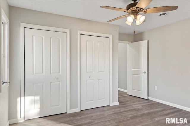 unfurnished bedroom featuring light hardwood / wood-style floors, ceiling fan, and multiple closets