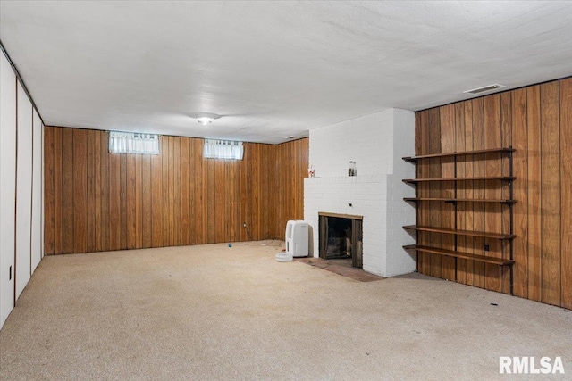 unfurnished living room featuring wood walls, light colored carpet, a textured ceiling, and a brick fireplace