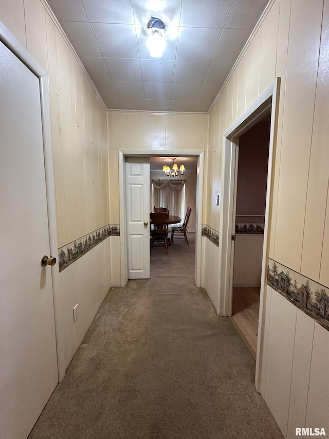 hall featuring carpet, ornamental molding, and a notable chandelier