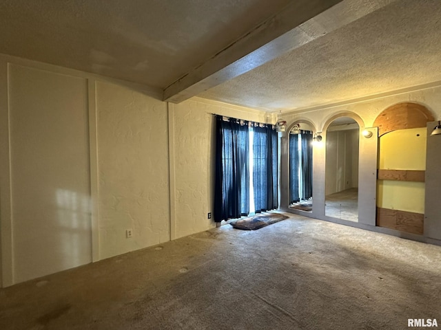 carpeted empty room featuring beamed ceiling and a textured ceiling