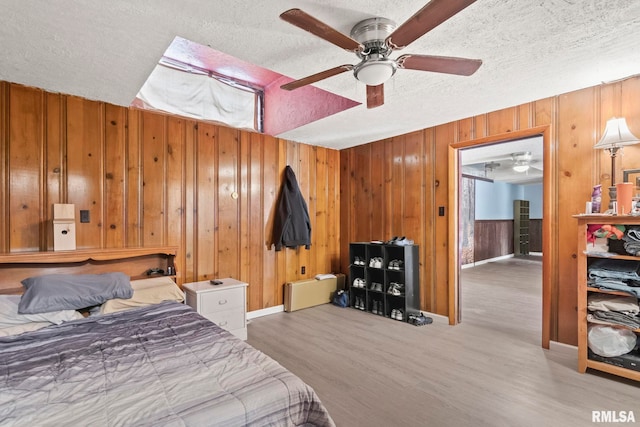 bedroom featuring ceiling fan, wooden walls, a textured ceiling, and light hardwood / wood-style flooring