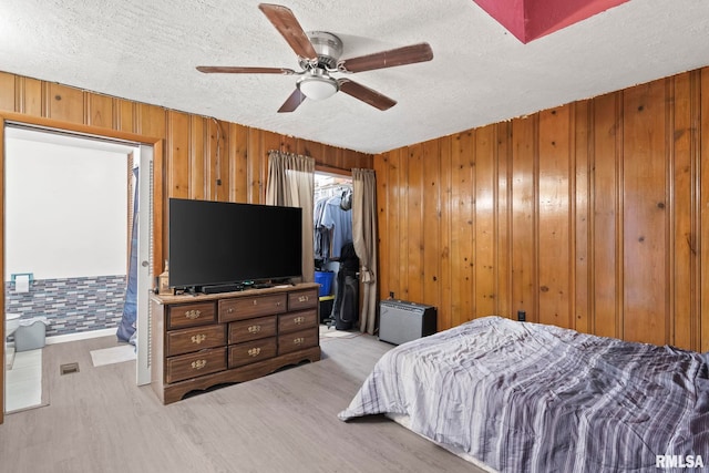 bedroom featuring light hardwood / wood-style flooring, a textured ceiling, a spacious closet, a closet, and wood walls