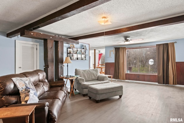 living room featuring beamed ceiling, ceiling fan, hardwood / wood-style flooring, and a textured ceiling