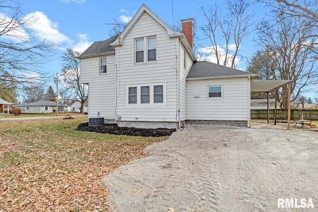 rear view of property featuring a carport, a yard, and central AC