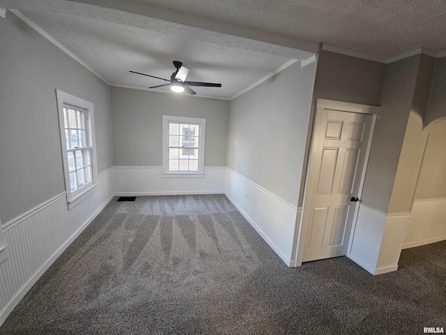 spare room with dark colored carpet, ceiling fan, ornamental molding, and a textured ceiling