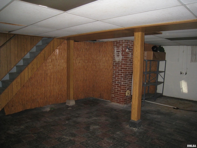 basement featuring a paneled ceiling and wooden walls