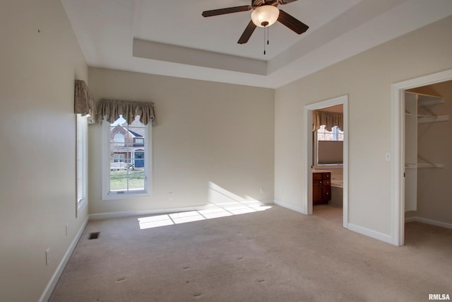 unfurnished bedroom with a tray ceiling, light colored carpet, a spacious closet, connected bathroom, and a closet