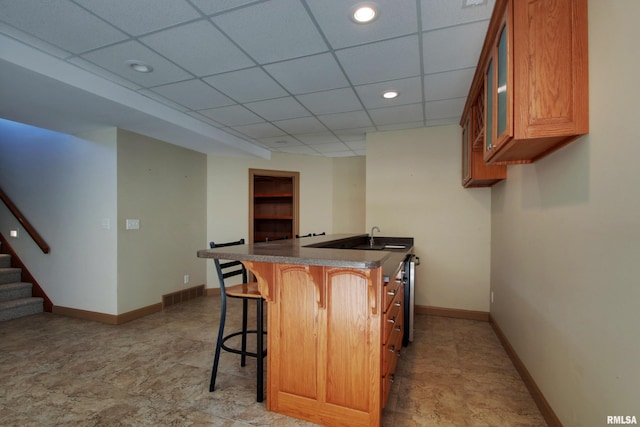 kitchen featuring a drop ceiling, sink, stainless steel dishwasher, kitchen peninsula, and a breakfast bar area