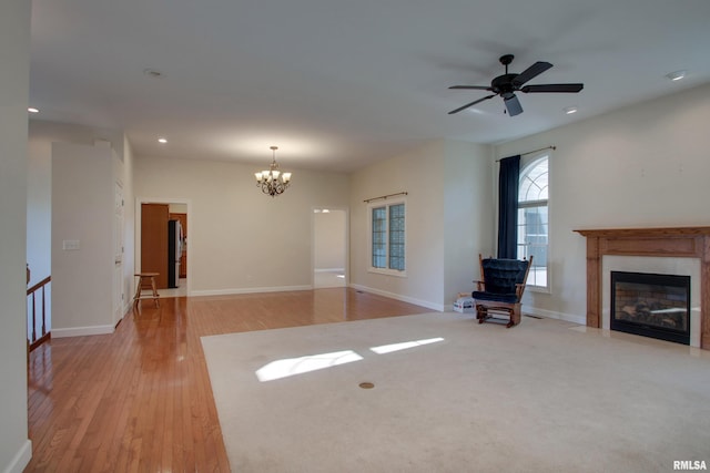 unfurnished living room featuring ceiling fan with notable chandelier and light wood-type flooring