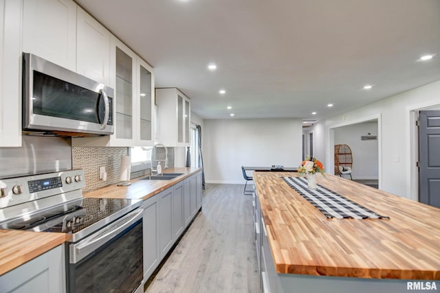 kitchen with appliances with stainless steel finishes, butcher block countertops, white cabinets, light hardwood / wood-style floors, and backsplash