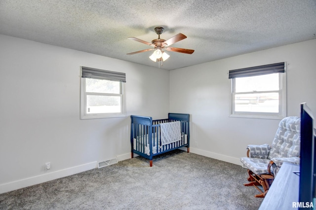 bedroom with multiple windows, a crib, carpet flooring, and a textured ceiling