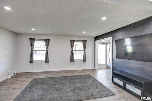 unfurnished living room featuring wood-type flooring, a textured ceiling, and a healthy amount of sunlight