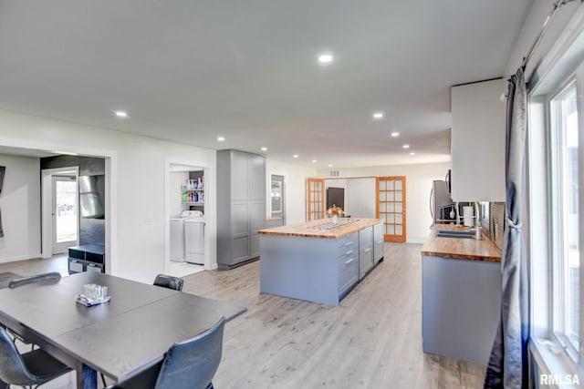 kitchen featuring light hardwood / wood-style flooring, washing machine and clothes dryer, butcher block countertops, a wealth of natural light, and gray cabinets